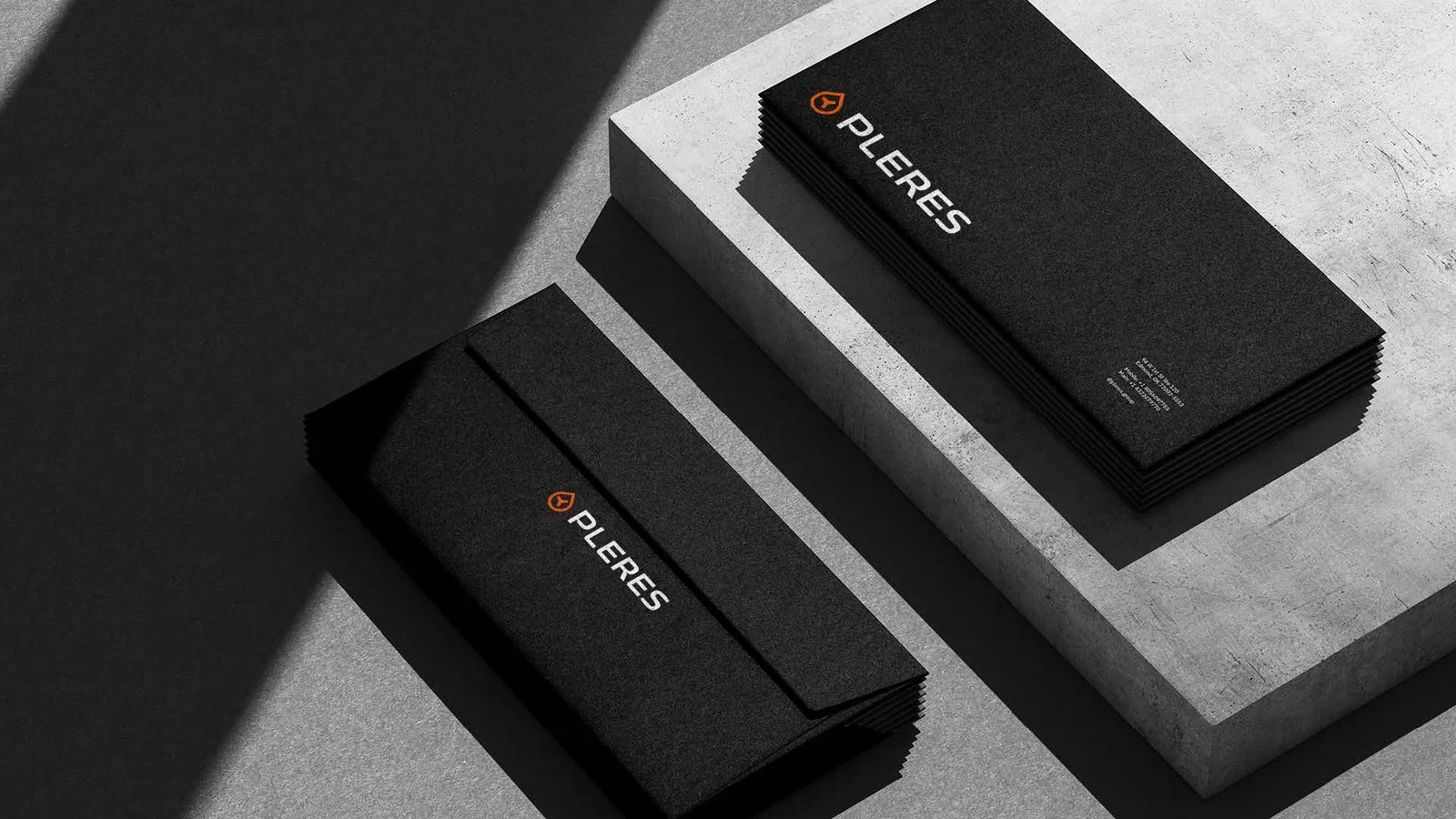 Stacks of black envelopes and letterhead on concrete, each printed with the orange brand mark and a white PLERES wordmark